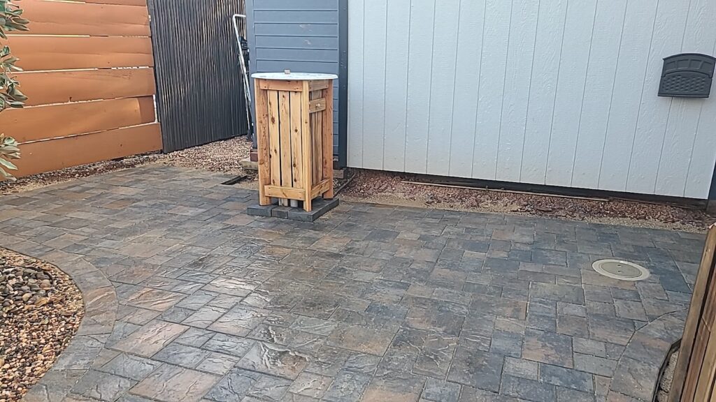 Outdoor patio area with brick pavers and a wooden cover beside a modern shed featuring a horizontal fence and gravel landscaping creating a clean minimalist look. - work by Mc Entire Landscaping in Redding, CA